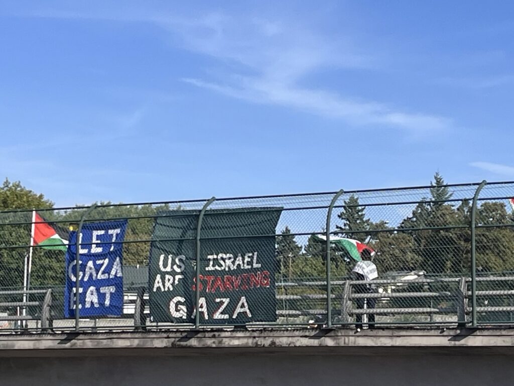 Activists displaying banners from a pedestrian bridge over a freeway. US/Israel Are Starving Gaza
Let Gaza Eat. 